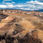 Panorama mozzafiato del paese piemontese con colline verdi e cieli azzurri.